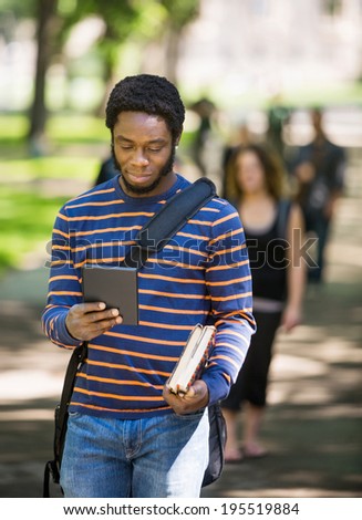 Young male student using digital tablet on campus with friends in background