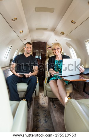 Portrait of confident business people with laptop and digital tablet in corporate jet