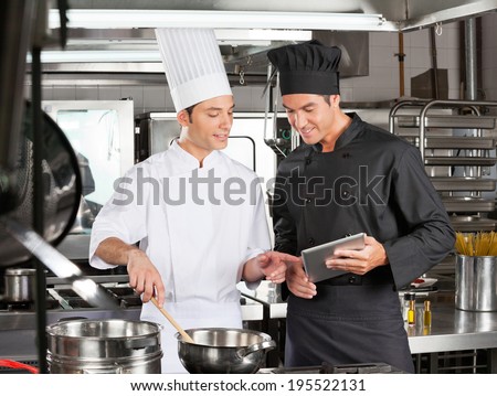 Young male chefs looking at digital tablet while preparing food in restaurant kitchen