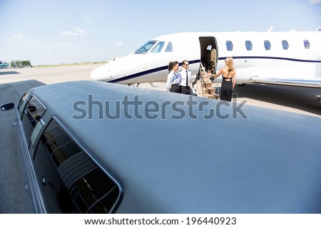 Woman boarding private jet with limousine in foreground at airport terminal