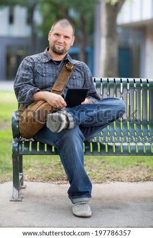 Portrait of confident male university student sitting on bench at university campus