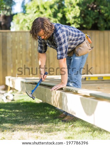 Mid adult manual worker using hammer on wooden frame at construction site