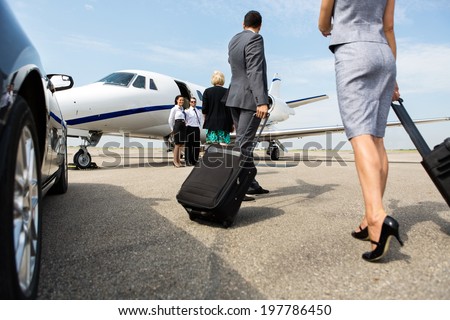 Business partners with luggage walking towards private jet at terminal