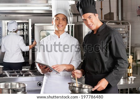 Portrait of happy chefs with digital tablet cooking in industrial kitchen
