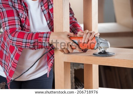 Midsection of female carpenter using sander on wooden shelf in workshop