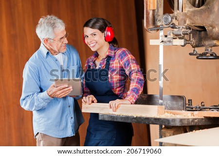 Portrait of young female carpenter with senior colleague using digital tablet in workshop