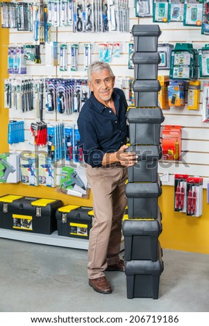 Full length of smiling senior man stacking toolboxes in hardware store