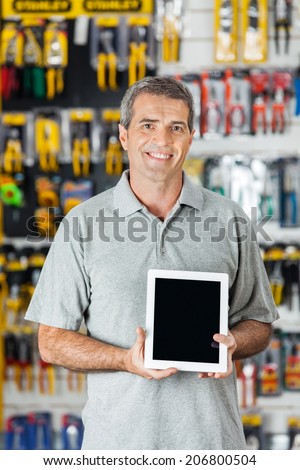 Portrait of confident mature man displaying digital tablet in hardware store