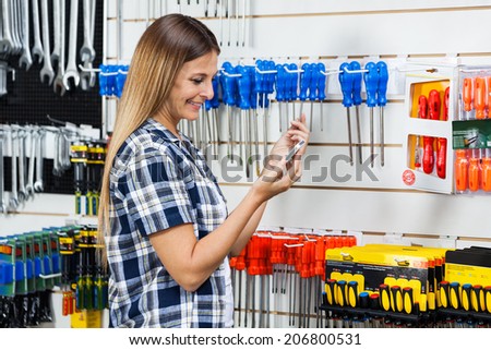 Side view of female customer checking information of screwdriver on mobilephone in hardware store