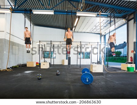 Full length of young male athletes exercising on gymnastic rings at gym