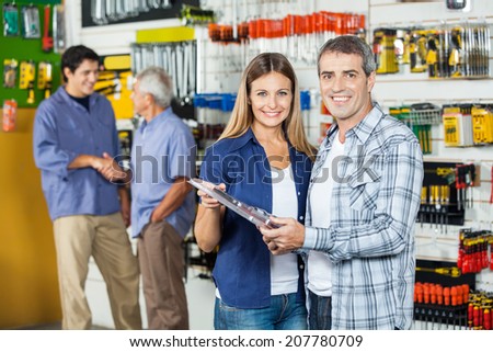 Portrait of happy couple buying tool set in hardware store with people hand shaking in background