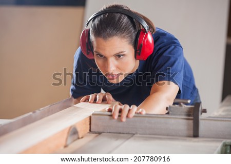 Concentrated young female carpenter cutting wood with tablesaw in workshop