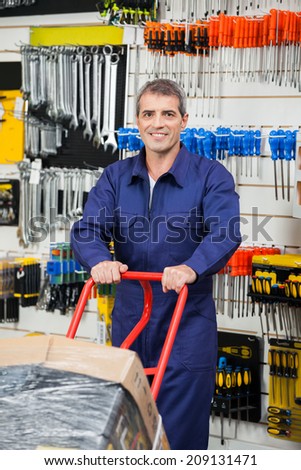 Portrait of mature worker in overalls pushing trolley in hardware shop