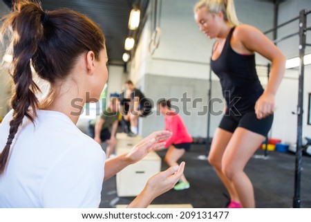 Female gym instructor encouraging athlete in box jumping at gym