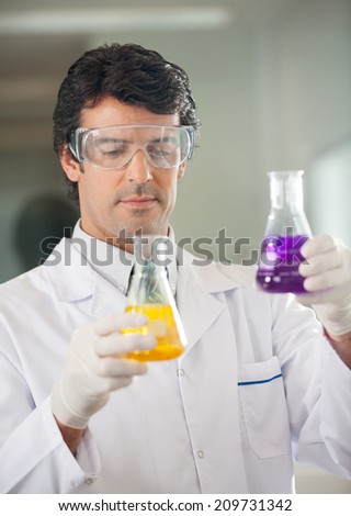 Mid adult male scientist examining flasks with different chemicals in lab