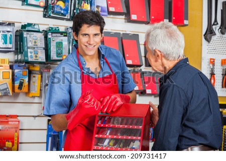 Portrait of smiling young salesman showing drill bit to senior man in hardware store