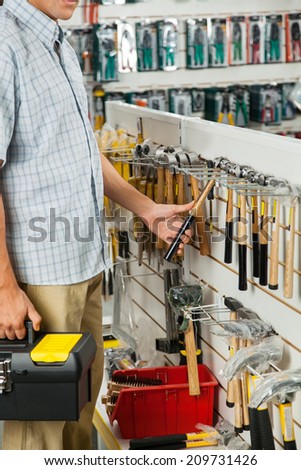 Midsection of young man examining hammer in hardware store