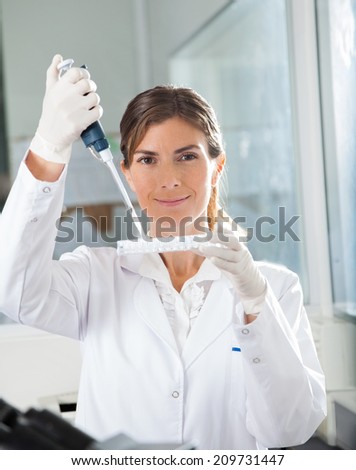 Portrait of young female scientist filling liquid into microplate in medical laboratory