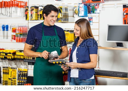 Happy woman holding screwdriver set with worker swiping credit card at hardware store