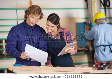 Male and female carpenters holding digital tablet and documents in workshop