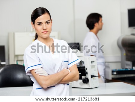 Portrait of confident young female scientist with colleague in background at laboratory