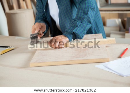 Midsection of senior male carpenter cutting wood with small saw at workbench