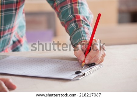Cropped image of carpenter writing notes on clipboard at table in workshop