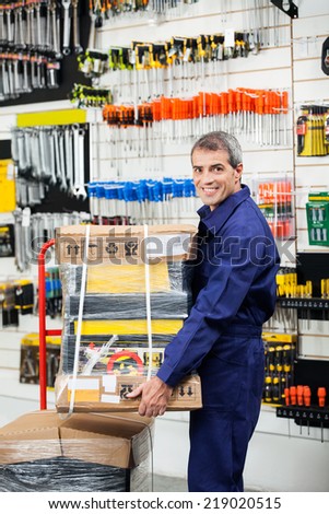 Side view portrait of mature worker keeping tool package on trolley in hardware shop