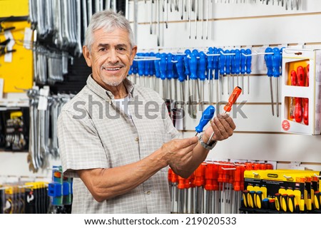 Portrait of happy senior customer comparing screwdrivers in hardware shop