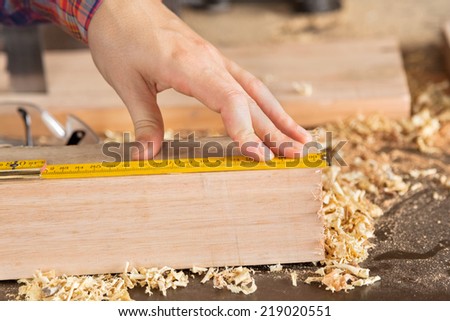 Closeup of female carpenter\'s hand measuring wood with scale in workshop