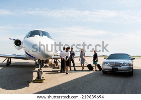 Business people with pilot and airhostess standing near private jet and limo at terminal