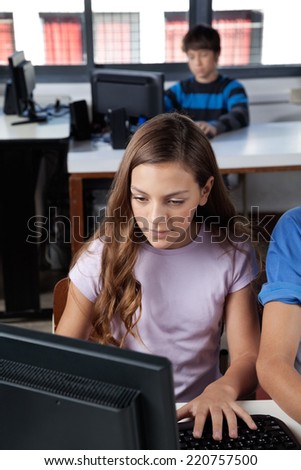 Teenage schoolgirl using computer at desk with classmate in background