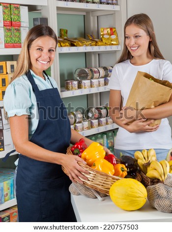 Portrait of saleswoman holding vegetable basket with female customer in supermarket