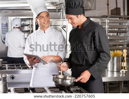 Male chef with digital tablet assisting colleague in preparing food at kitchen