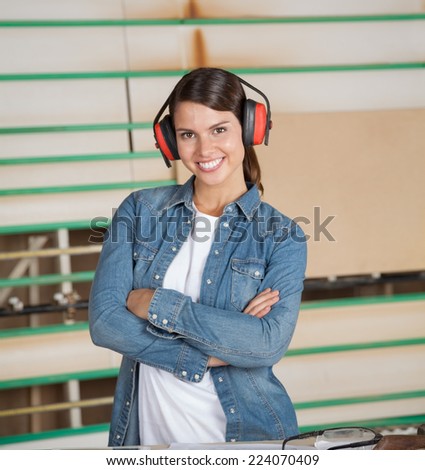 Portrait of confident female carpenter wearing ear protectors in workshop