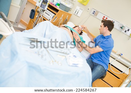 Couple in hospital with woman giving birth, surgical tools out of focus in foreground