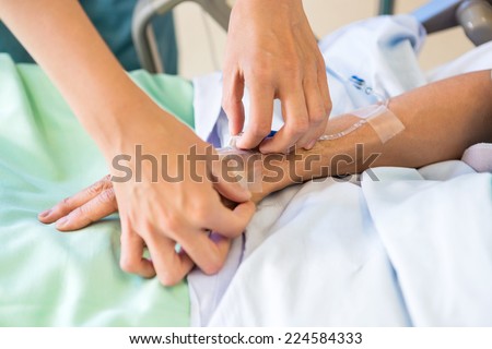 Cropped image of female nurse attaching IV drip on male patient\'s hand in hospital