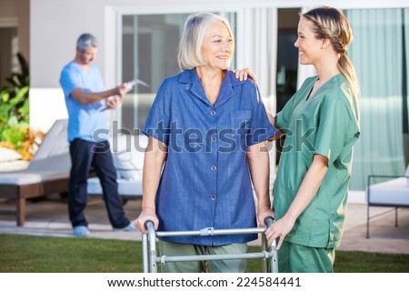 Smiling disabled senior woman and nurse looking at each other in lawn at nursing home