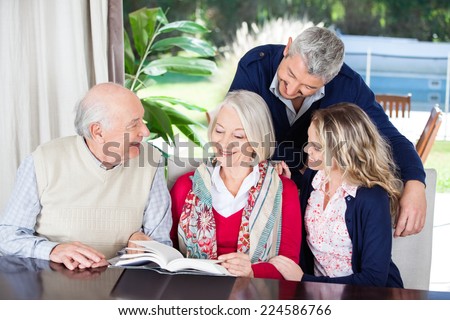 Happy couple looking at grandparents reading book while sitting in nursing home