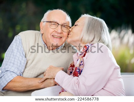 Senior woman kissing on man\'s cheek while sitting at nursing home porch
