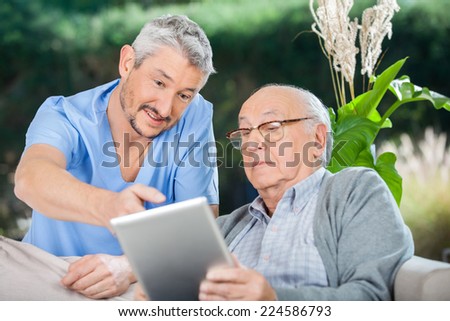 Male nurse showing something to senior man on digital tablet at nursing home porch