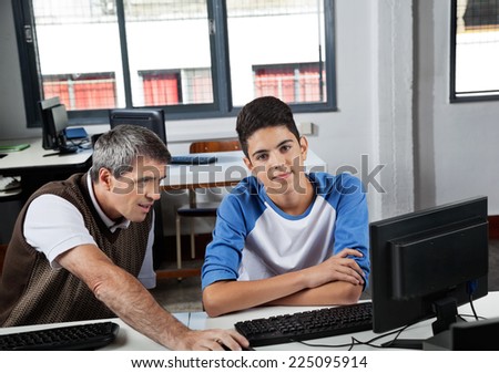 Portrait of teenage schoolboy with teacher using computer at desk in lab