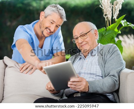 Happy male nurse helping senior man in using tablet computer at nursing home porch