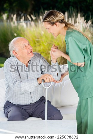 Side view of female nurse helping senior man to get up from couch