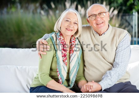 Portrait of happy senior man sitting with arm around woman on couch at nursing home porch