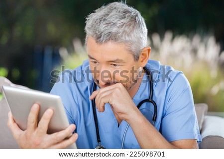 Male doctor using tablet PC while sitting at nursing home