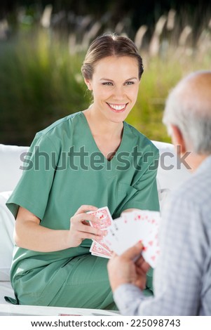 Beautiful female nurse playing cards with senior man at nursing home