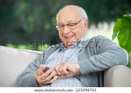 Smiling senior man text messaging through mobile phone at nursing home porch