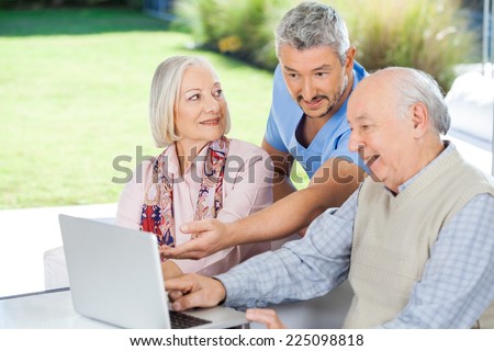 Male caretaker showing something to senior couple on laptop at nursing home