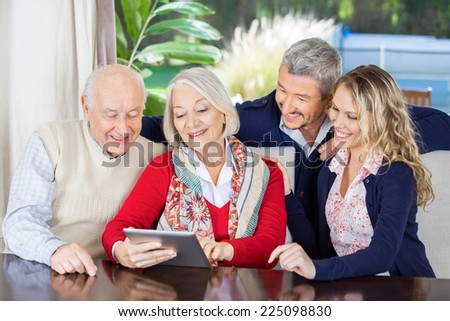 Happy grandchildren looking at grandparents using digital tablet in nursing home